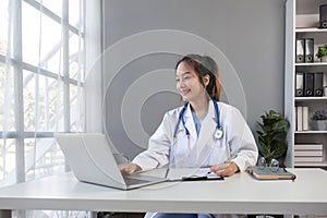 Asian doctor young beautiful woman smiling using working with a laptop computer and her writing something on paperwork