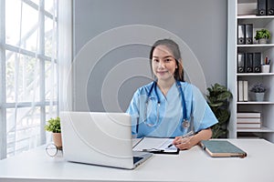 Asian doctor young beautiful woman smiling using working with a laptop computer and her writing something on paperwork