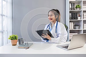 Asian doctor young beautiful woman smiling using working with a laptop computer and her writing something on paperwork