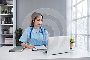 Asian doctor young beautiful woman smiling using working with a laptop computer and her writing something on paperwork
