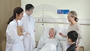 Asian doctors talking to senior patient and family members in hospital ward