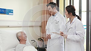 Asian doctors talking to senior patient in hospital ward