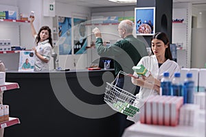 Asian druggist holding shop cart putting pills package in it