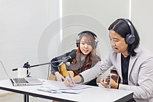 Asian duo rock band is composing song as the male member is writing lyrics on paper while working in small recording home studio