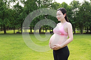 Asian Eastern Chinese happy pregnant woman in yoga dress hands hold her belly expecting baby to born parents mother love concept