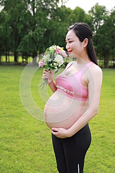 Asian Eastern Chinese happy pregnant woman in yoga dress hands hold her belly expecting baby to born smell flowers hold bouquet