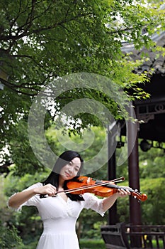 Asian Eastern Chinese young artist player woman carry play violin perform enjoy music in park garden outdoor nature