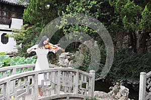 Asian Eastern Chinese young artist player woman carry play violin perform music park garden nature ancient building stand bridge