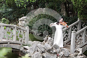 Asian Eastern Chinese young artist player woman carry play violin perform music park garden nature ancient building stand bridge