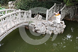 Asian Eastern Chinese young artist player woman carry play violin perform music park garden nature ancient building stand bridge