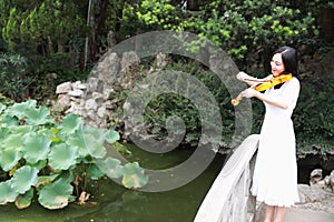 Asian Eastern Chinese young artist player woman carry play violin perform music park garden nature ancient building stand bridge