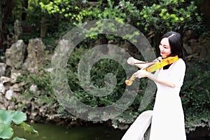 Asian Eastern Chinese young artist player woman carry play violin perform music park garden nature ancient building stand bridge