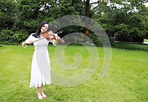 Asian Eastern Chinese young artist player woman carry play violin stand on green grass meadow bare feet performance in a park free