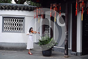 Asian Eastern Chinese young artist player woman play violin perform music garden nature outdoor ancient building red lantern