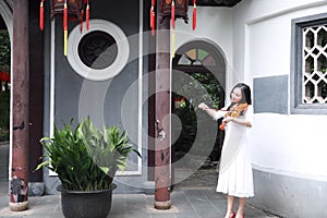 Asian Eastern Chinese young artist player woman play violin perform music garden nature outdoor ancient building red lantern