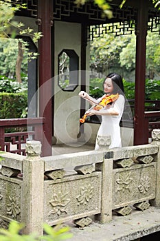 Asian Eastern Chinese young artist player woman play violin perform music park garden nature outdoor ancient building bridge