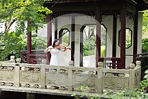 Asian Eastern Chinese young artist player woman play violin perform music pavilion garden nature outdoor ancient building bridge