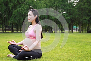 Asian Eastern Chinese young pretty pregnant girl woman do yoga sit in meditation, do lotus gesture of yoga closed-eyes over sunset