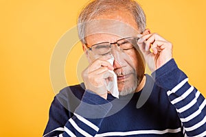 Asian elder man crying raise glasses with tissue wipe red eyes