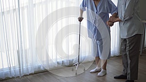 Asian elder senior husban help wife practice walking use stick physical theraphy to recover leg injure