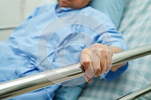 Asian elder senior woman patient holding bed rail while lie down with hope waiting her family in hospital