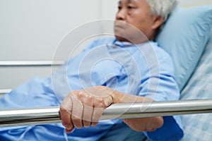 Asian elder senior woman patient holding bed rail while lie down with hope waiting her family in hospital