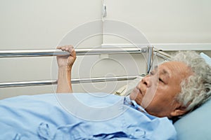 Asian elder senior woman patient holding bed rail while lie down with hope waiting her family in hospital