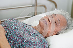 Asian elder senior woman patient holding bed rail while lie down with hope waiting her family in hospital