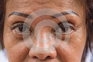 Asian elder women show her eyes and eyebrow tattoo