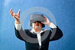 Asian elderly business woman Wearing virtual reality VR glasses, hands stretched forward, blue background.