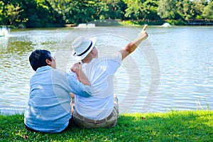 Asian elderly couple enjoying a good day sitting on the grass by the pool in the park.