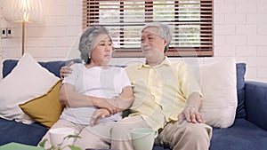 Asian elderly couple feeling happy smiling and looking to camera while relax on the sofa in living room at home.