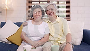 Asian elderly couple feeling happy smiling and looking to camera while relax on the sofa in living room at home.
