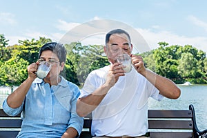 Asian elderly couple sitting, holding glass and drinking milk