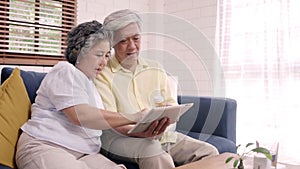 Asian elderly couple using tablet search medicine information in living room, couple using time together while lying on sofa when