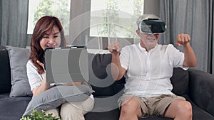 Asian elderly couple using tablet and virtual reality simulator playing games in living room, couple feeling happy time together