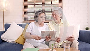 Asian elderly couple using tablet watching TV in living room at home.