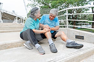 Asian elderly couple, wife touches and looking at her husband's knee, which is injuries from exercise.