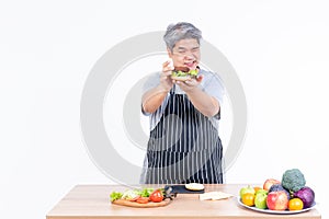 Asian elderly man is cooking a hamburger Which contains fresh vegetables, meat and cheese