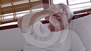 Asian Elderly man with a headache sitting on a bed in morning