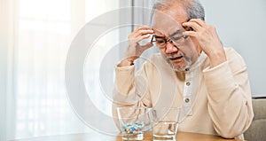 Asian elderly man sick have headache looking pill glass on at home