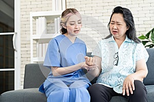 Asian elderly senior woman clenched her hands tightly and cute nurse hold senior woman hand and suggests during physical therapy