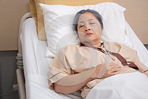 Asian elderly woman asleep on bed with surveillance in hospital ward, patient senior unconscious lying on bed.