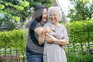 Asian elderly woman with caregiver daugther walking and hug with happy in nature park