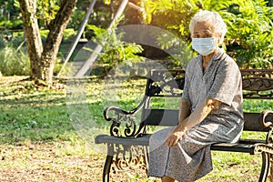 Asian elderly woman depressed and sad with mask for protect covid 19 sitting back on bench in autumn park