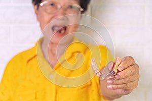 Asian Elderly woman over 70 years old be smile with a few broken teeth and holding dentures in hand. Dentures for prosthetic devic