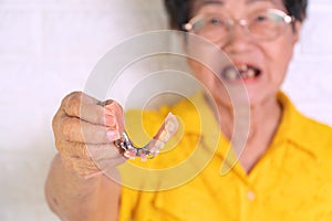 Asian Elderly woman over 70 years old holding dentures in hand. Dentures for prosthetic devices constructed to replace missing tee