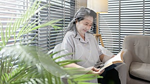 Asian elderly woman is reading book , relaxing at home , senior health care concept