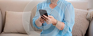 Asian elderly woman using smartphone to social media online sitting on sofa with relax in living room.