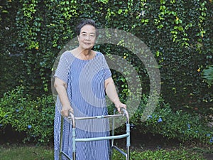 Asian elderly woman walking with orthopedic walker in the garden. Physical activity of old age concept
